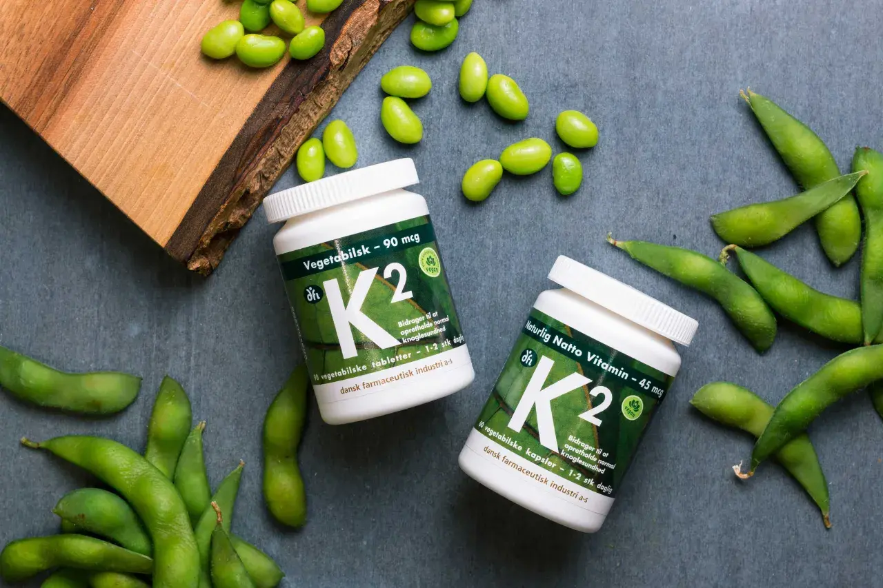 Zwei Flaschen Vitamin K2, umgeben von frischen Edamame-Bohnen. Vegane K2-Lebensmittel für gesunde Knochen.