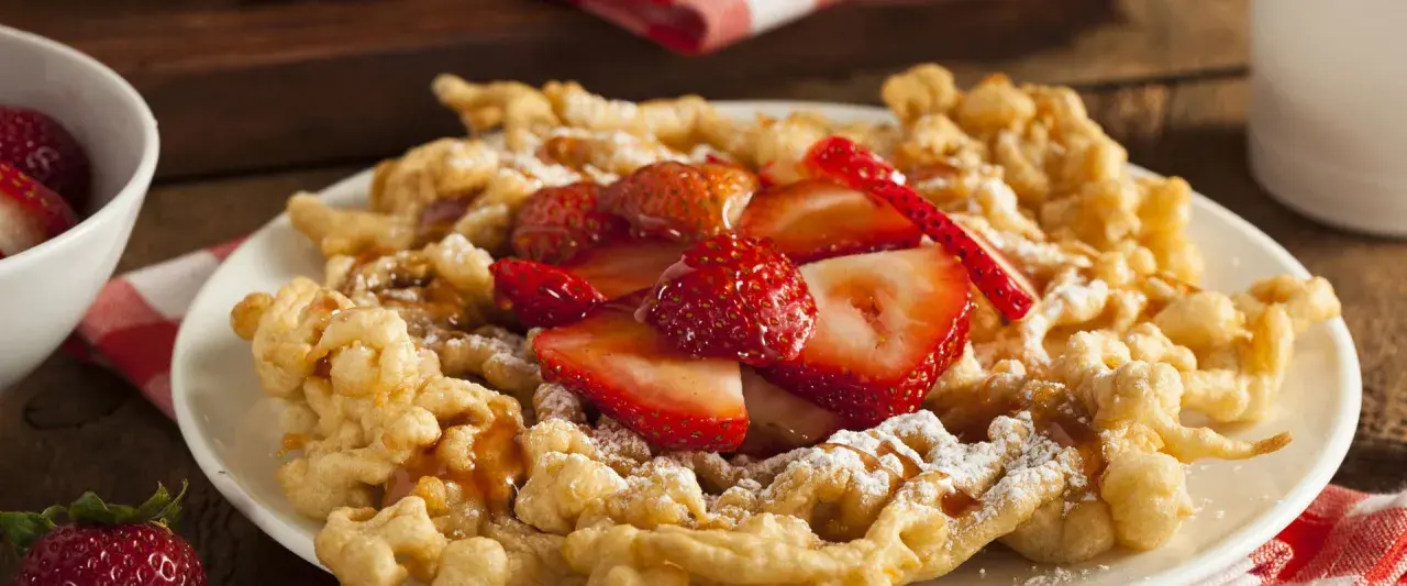 Strauben croccanti, guarniti con fragole fresche e zucchero a velo. Una deliziosa ricetta per un dolce da fiera.