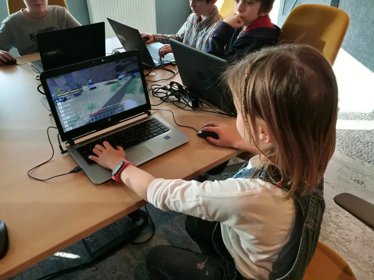 Dzieci grają w grę komputerową na laptopach podczas lekcji kodowania.