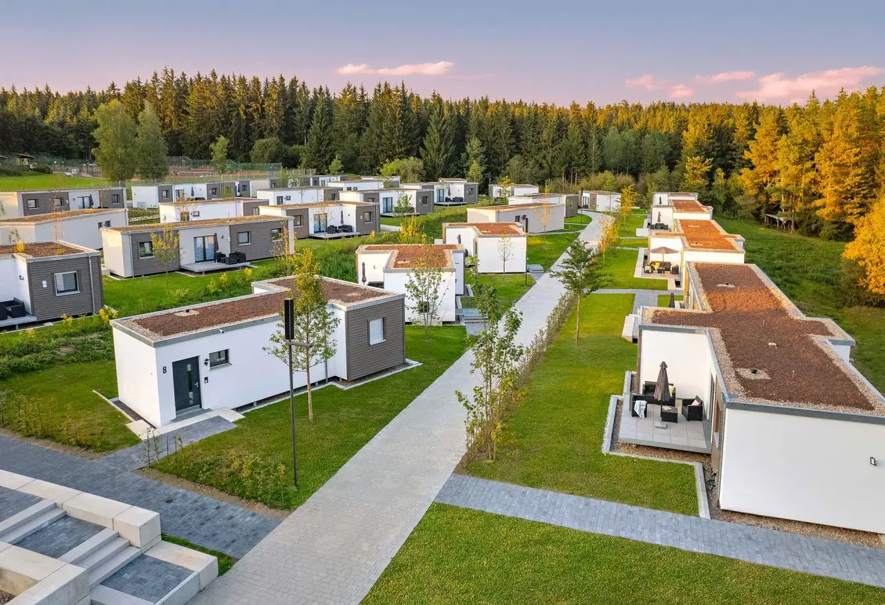 Reihe von kleinen Häusern, modern und minimalistisch, mit begrünten Dächern, eingebettet in eine grüne Landschaft am Waldrand.