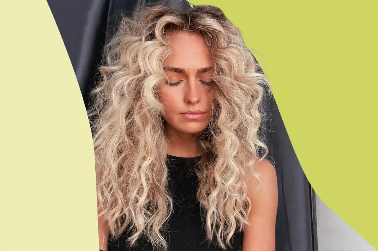 Mujer con cabello rubio, rizado y esponjoso, con los ojos cerrados y un ligero bronceado.