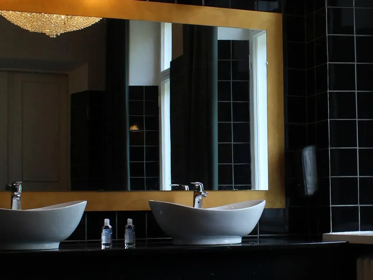 Elegante bagno nero design con due lavabi bianchi, rubinetteria cromata e specchio dorato. Pareti rivestite di piastrelle nere lucide.