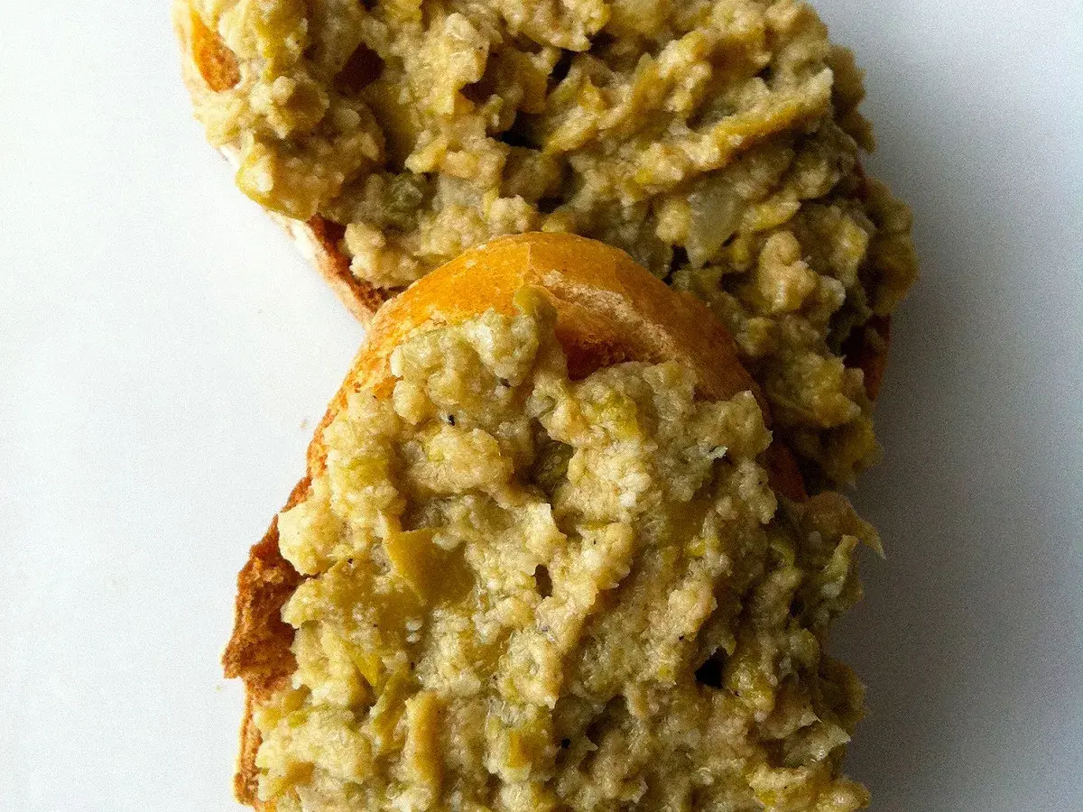 Deux tranches de pain garnies d'une généreuse portion de tapenade verte, prêtes à être dégustées.