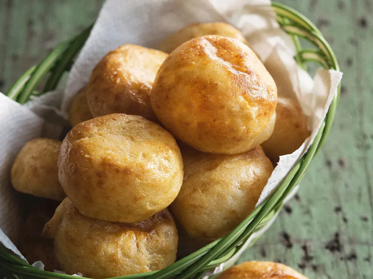 Petits pains dorés, une délicieuse recette de manioc, servis dans un panier en osier garni de papier blanc.