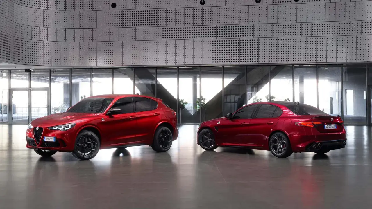 Dwa czerwone Alfa Romeo, SUV Stelvio i sedan Giulia Quadrifoglio, stoją obok siebie w nowoczesnym wnętrzu.