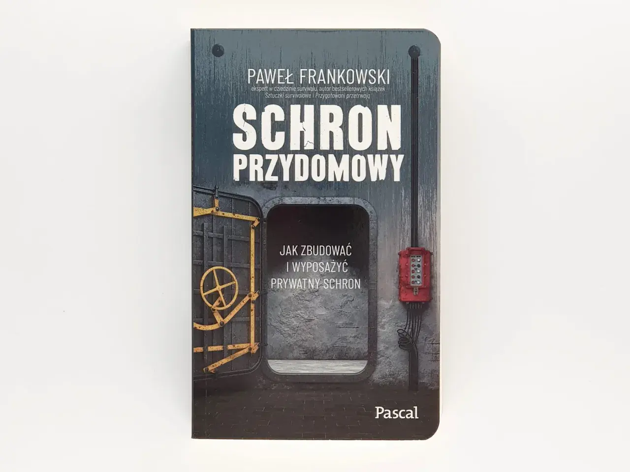 Okładka książki "Schron przydomowy" Pawła Frankowskiego. Przedstawia wejście do schronu z żółtą kierownicą i czerwoną skrzynką elektryczną.