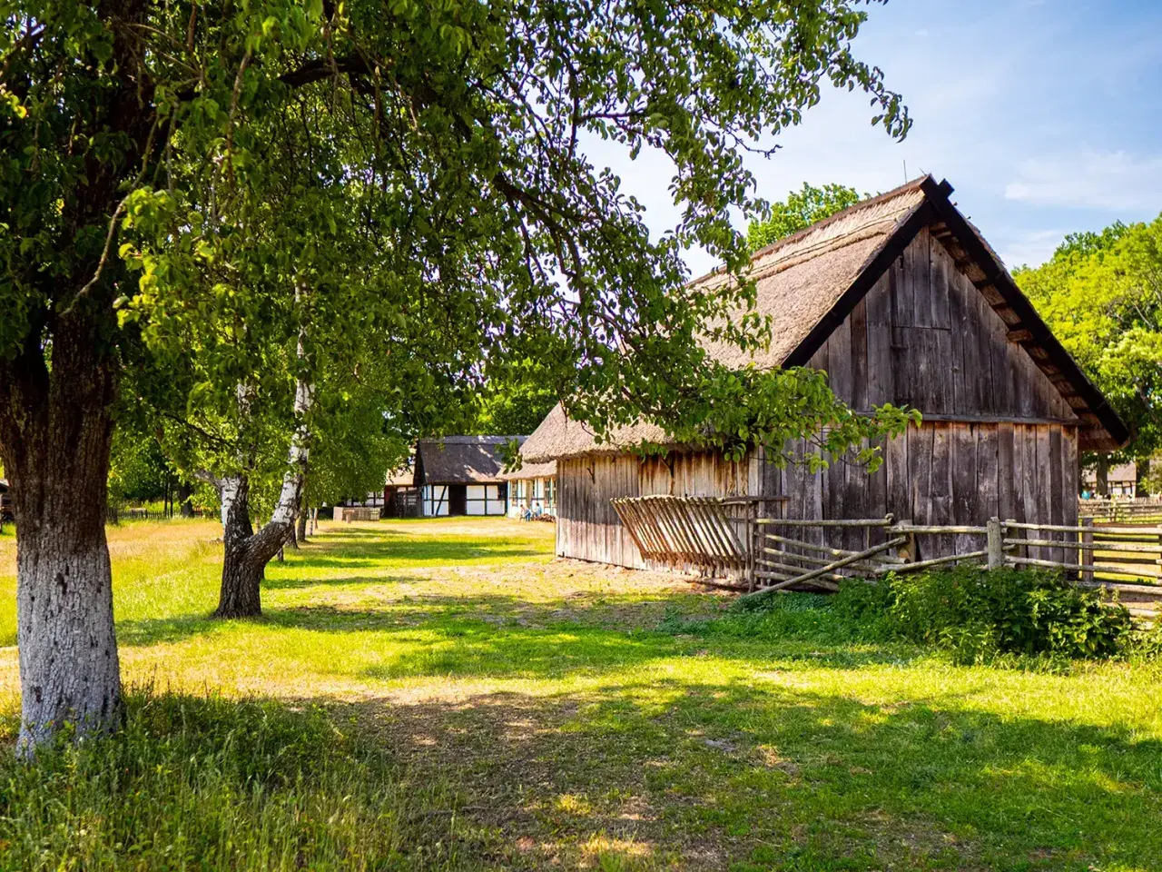 Skansen w Klukach: drewniane chaty z krytymi strzechą dachami, otoczone zielenią i sielskim krajobrazem.