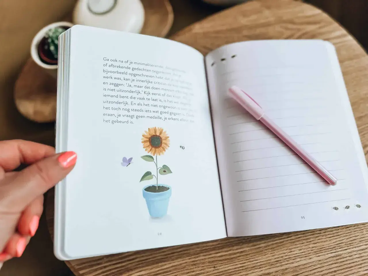 Een open dagboek met een zonnebloem en vlinder illustratie. Een roze pen ligt op de rechterpagina, klaar om gedachten uit je hoofd op te schrijven.