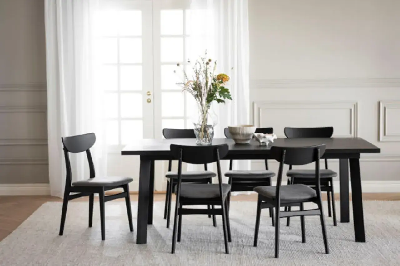 Ett modernt matbord med sex svarta stolar. Utrymme runt matbordet är inrett med en vas med blommor och en skål.