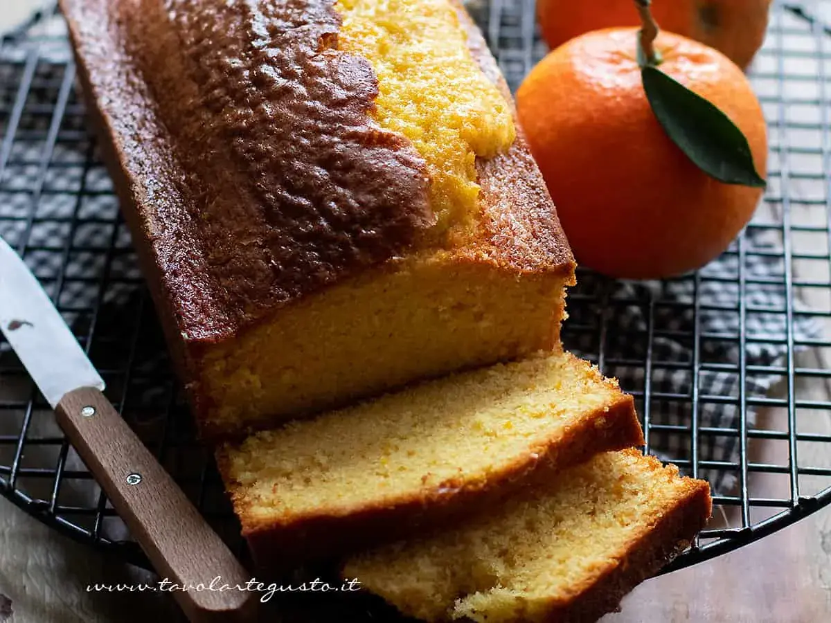 Plumcake all'arancia appena sfornato, dorato e profumato, con fette morbide e arance fresche accanto.