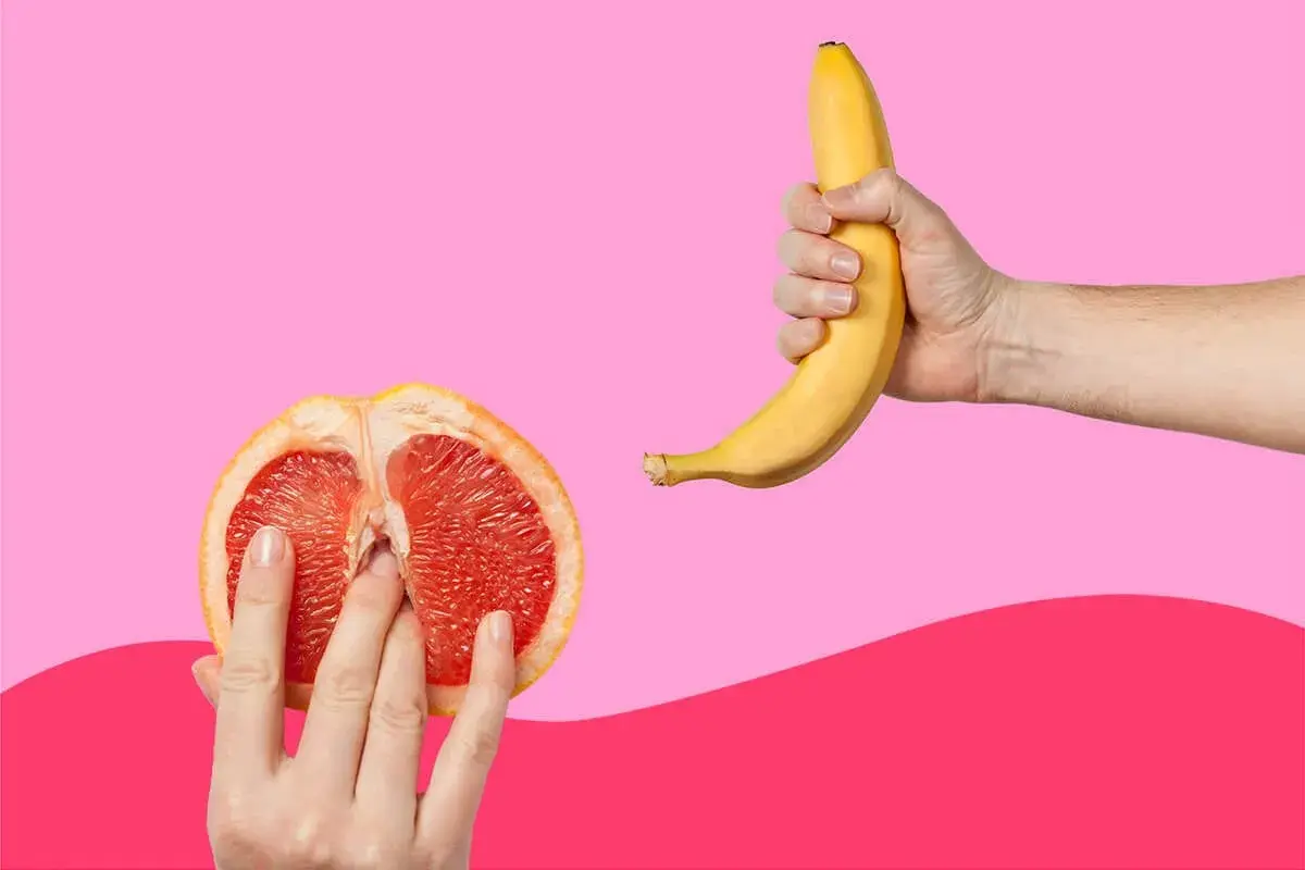 Mani che esplorano un pompelmo tagliato a metà, suggerendo come ci si masturba, mentre una banana è tenuta in un'altra mano.