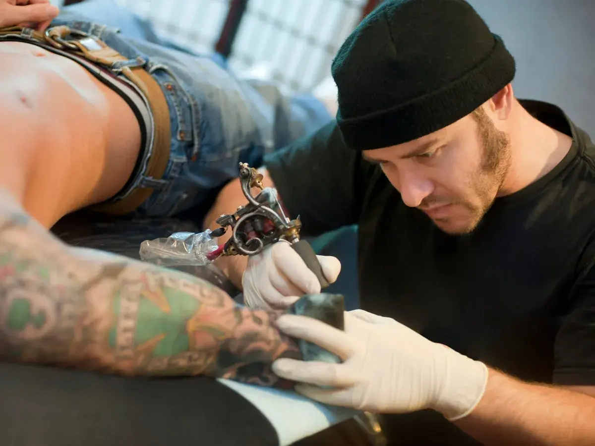 Artista de tatuajes concentrado, considerado el mejor del mundo, trabajando en un brazo con diseño detallado.