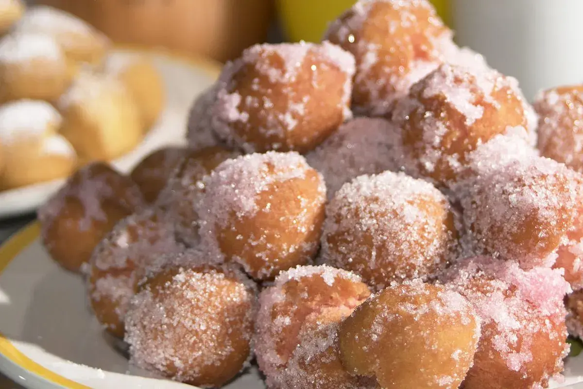 Castagnole marchigiane ricetta originale: dolcetti fritti dorati, cosparsi di zucchero semolato e un tocco di zucchero rosa.