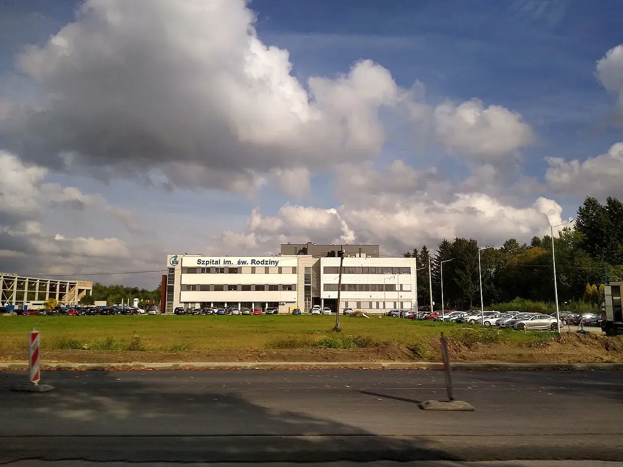 Szpital im. Św. Rodziny, dojazd autobusem. Budynek szpitala z parkingiem i zielenią.
