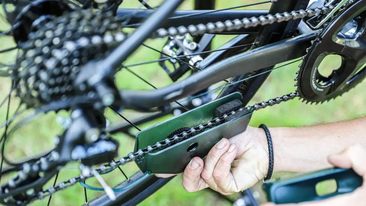 Czyszczenie łańcucha rowerowego za pomocą specjalnego narzędzia. Widać mechanizm przerzutek i zębatki.