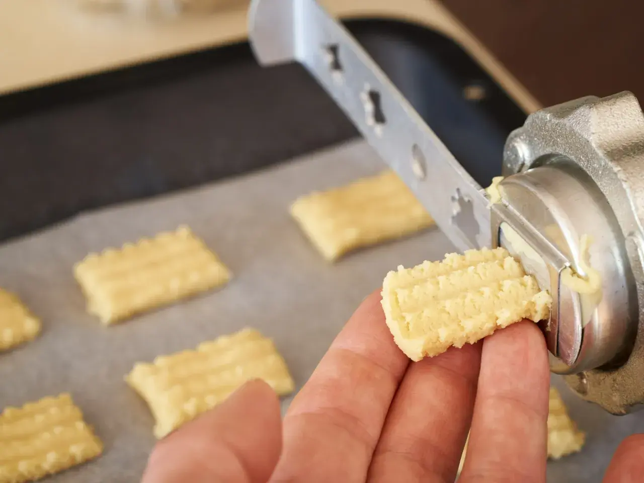 Ręka trzyma świeżo wyciśnięte ciastka z maszynki, gotowe do pieczenia.