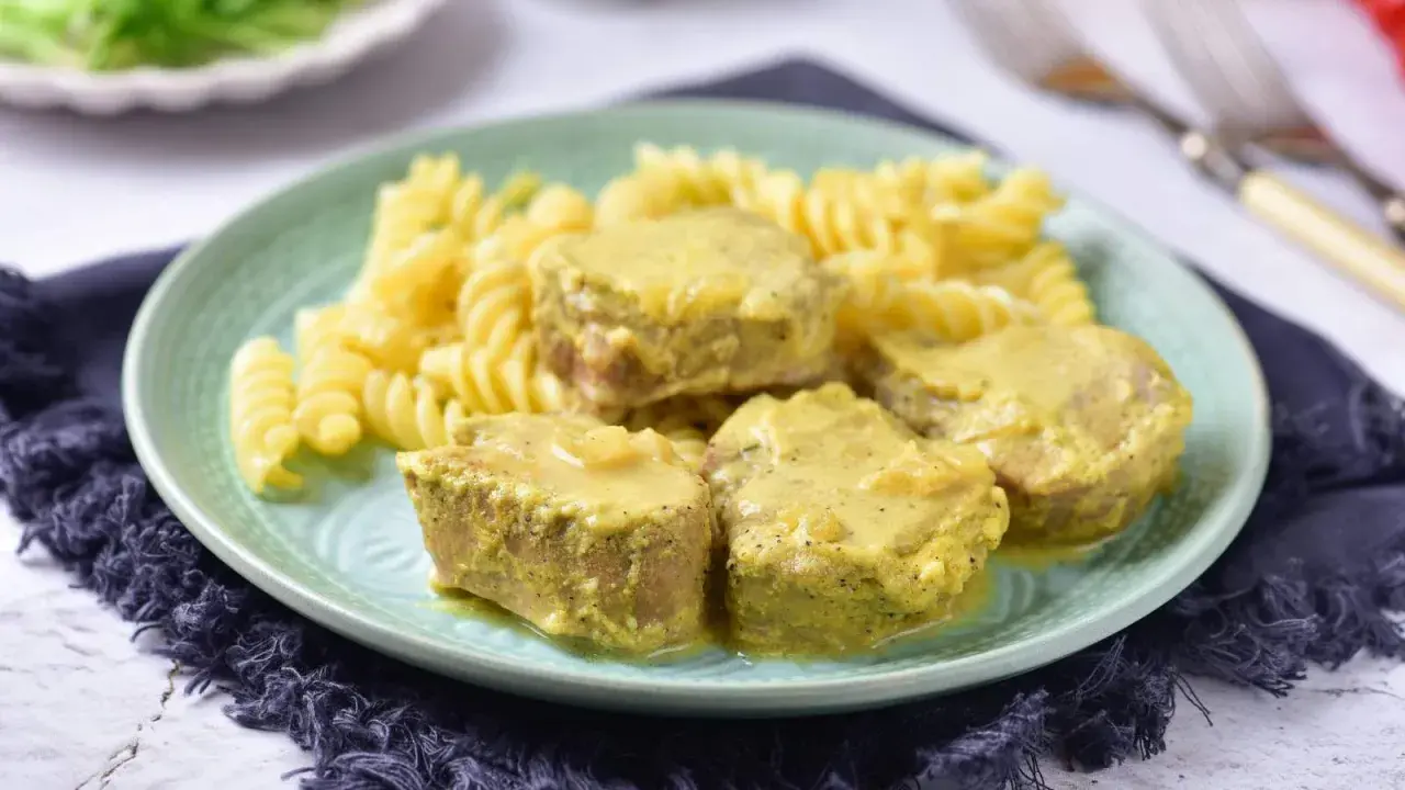Soczyste polędwiczki w sosie musztardowym podane z makaronem fusilli na zielonym talerzu.