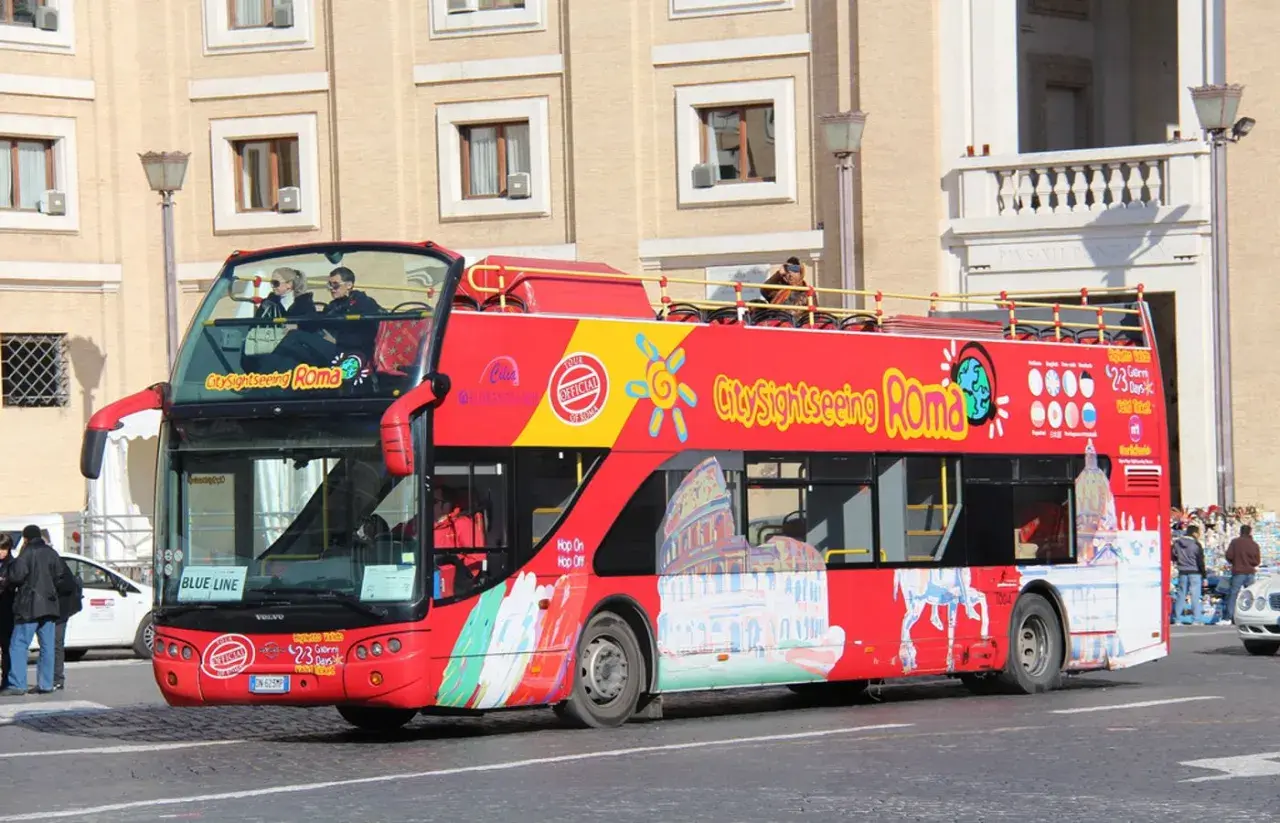 Un bus rouge à deux étages, un bus touristique "City Sightseeing Roma", circule dans la ville.