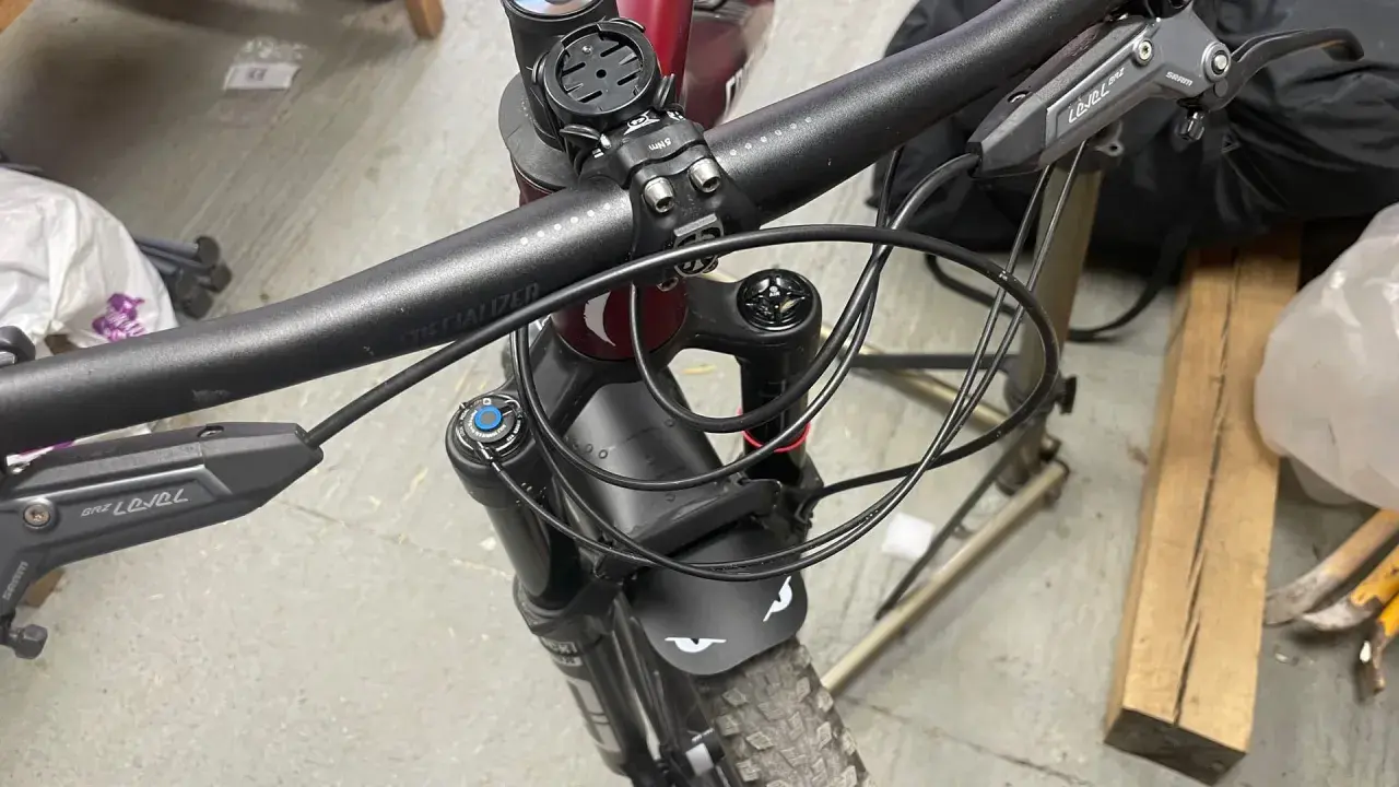 Close-up of a mountain bike's handlebars and front fork, showing the brake levers and the neat routing of the cutting hydraulic hose.