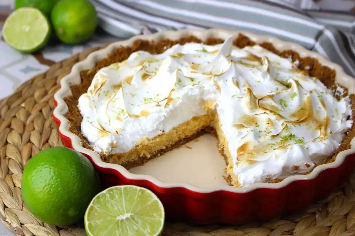 Delicioso key lime pie con merengue dorado y ralladura de lima, acompañado de limas frescas.