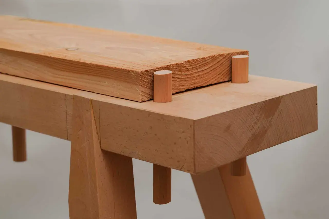 Holzverbindung für eine Werkbank selbst bauen: Ein Holzbalken ruht auf zwei Holzdübeln, die in einer weiteren Holzplatte stecken.