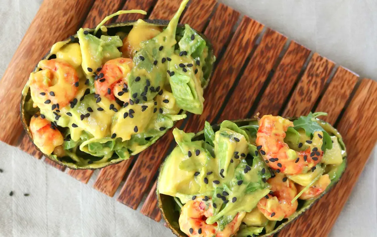 Deliciosa ensalada de langostinos y aguacate, servida en mitades de aguacate y espolvoreada con semillas de sésamo negro.
