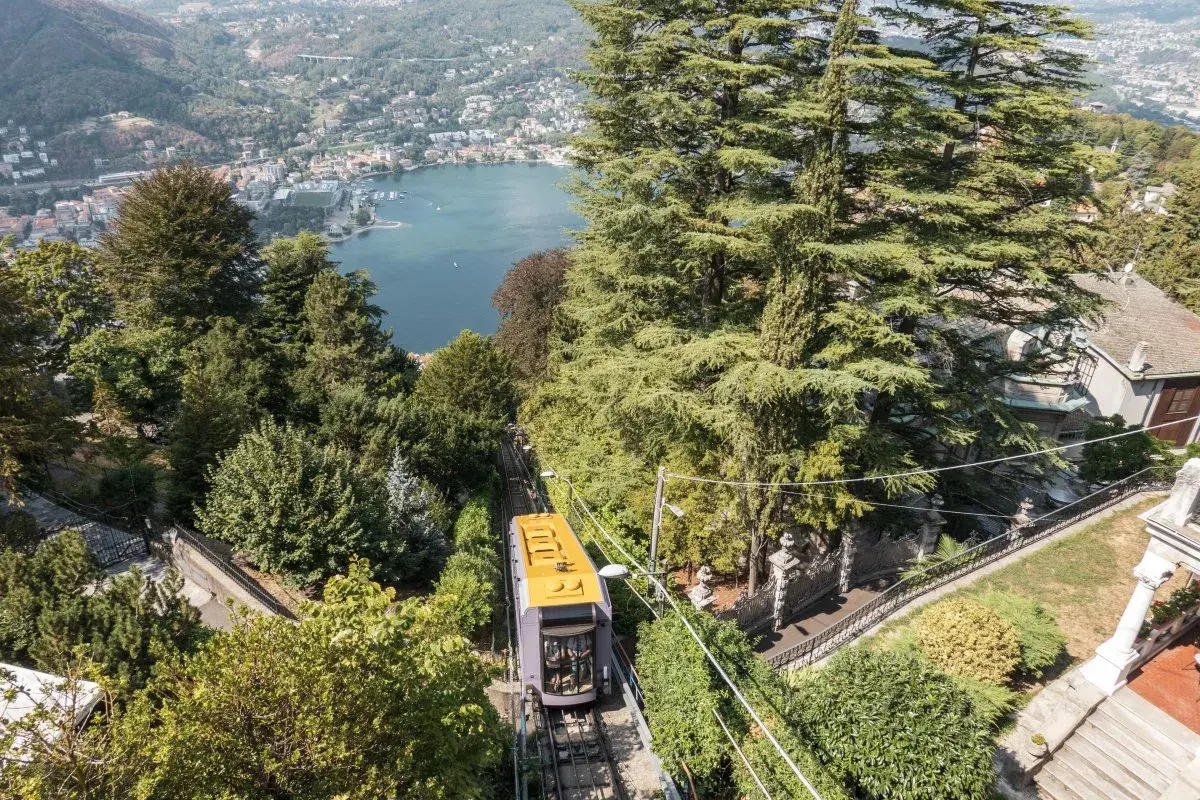 Gelbe Standseilbahn fährt bergauf, Blick auf Comer See und Bahnhof.