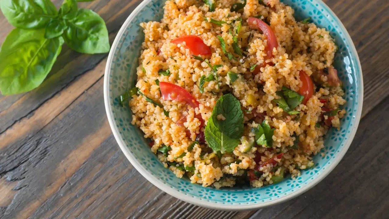 Una ciotola di insalata di cous cous con pomodorini e erbe fresche, pronta per essere gustata.