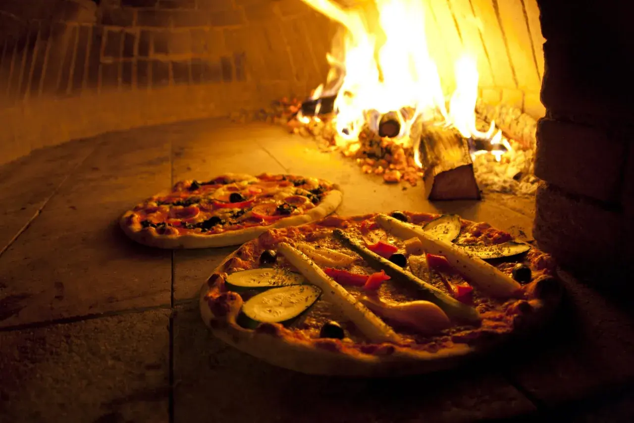 Zwei Pizzen im Holzofen, die Hitze des Feuers sorgt für die perfekte pizza ofen temperatur.