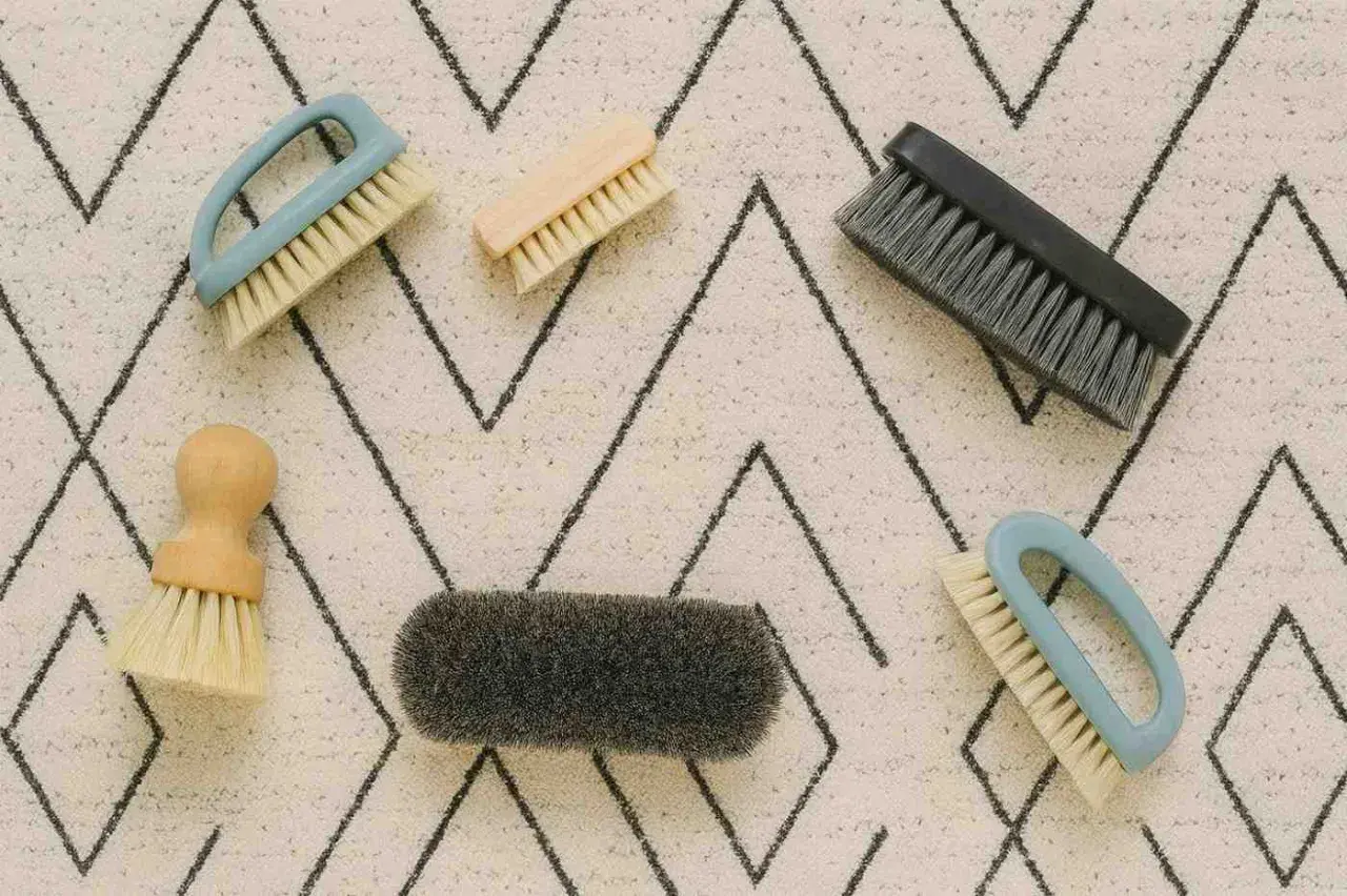 Cinco cepillos de diferentes tamaños y colores sobre una alfombra con patrón de zigzag. Herramientas perfectas para saber como limpiar alfombras a mano.