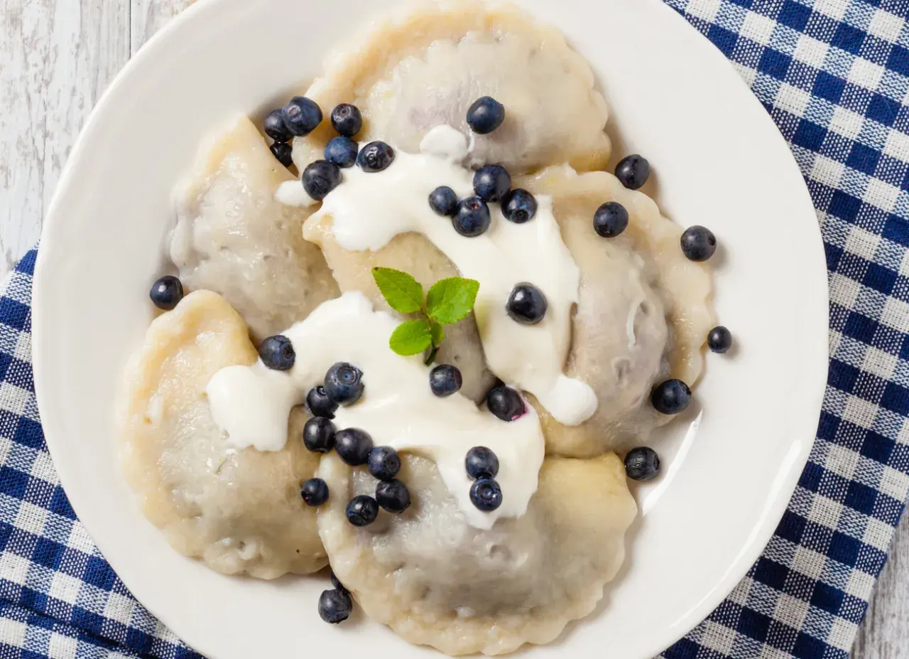 Pyszne pierogi z jagodami, polane śmietaną i posypane świeżymi owocami. Idealne na letni deser.