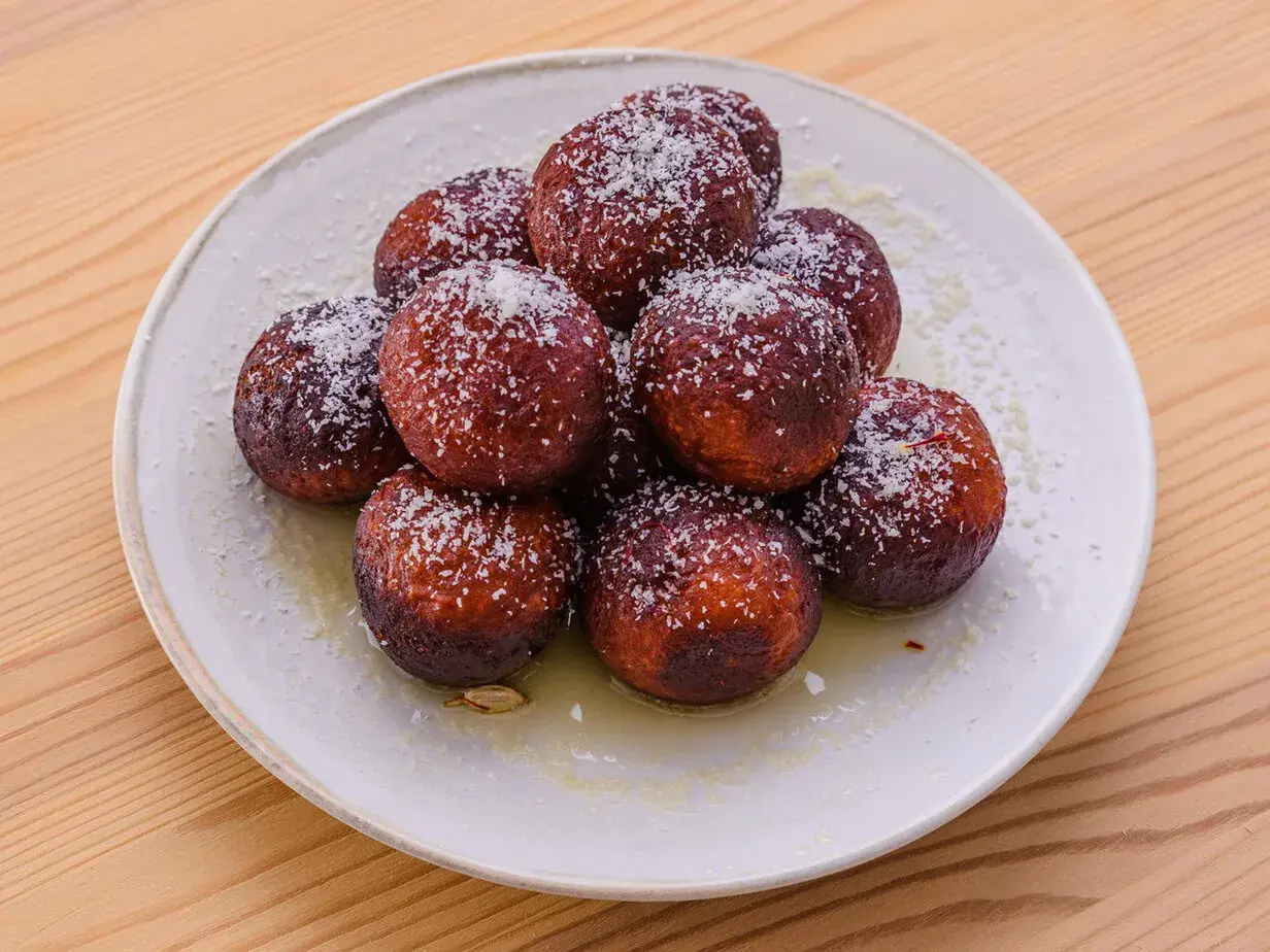 En hög med söta, mörka gulab jamun, pudrade med kokosflingor och serverade i en ljus sirap.