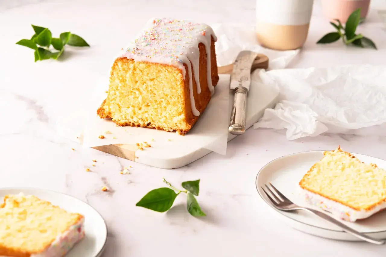 Ein saftiger Zitronenkuchen in Kastenform, mit Zuckerguss und bunten Streuseln verziert, wartet auf seine Genießer.