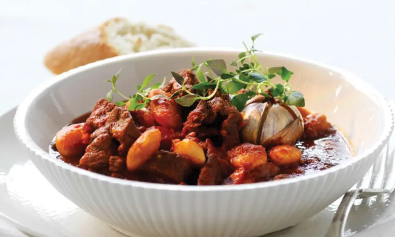 En skål med mustig chili con carne, garnerad med färska örter och en hel vitlöksklyfta. En bit bröd syns i bakgrunden.