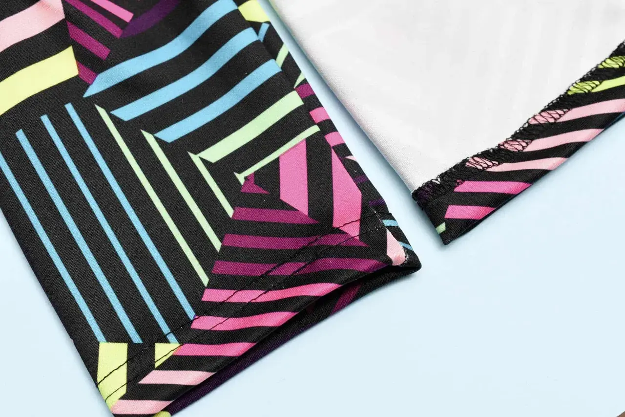 Close-up of colorful geometric leggings. The fabric is black with vibrant stripes of pink, blue, yellow, and green. The stitching shows how you can sew leggings.