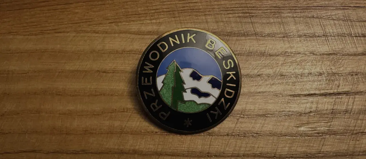 Odznaka z napisem "Przewodnik Beskidzki" i malowniczym krajobrazem górskim.