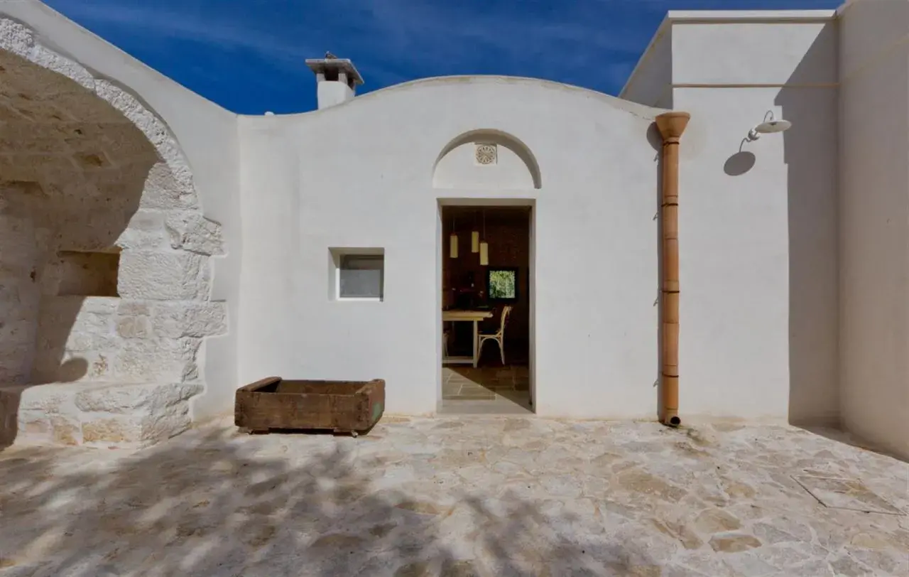Interni di trulli pugliesi: un'apertura bianca rivela una sala da pranzo accogliente, con un camino e un piccolo orto in pietra all'esterno.