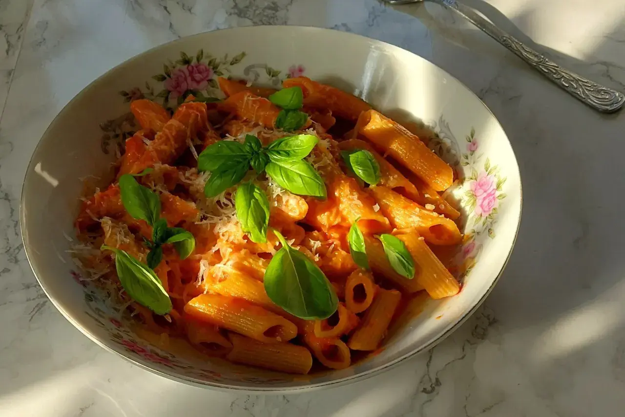 Penne arrabiata z bazylią i parmezanem, podane w ozdobnej misce.
