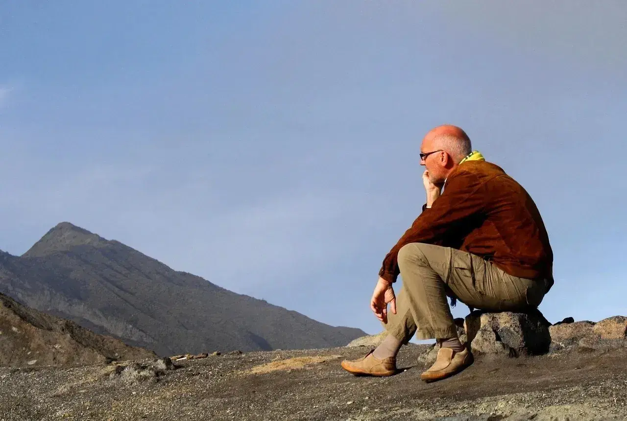 A man in hiking gear sits on a rock, contemplating the vast, barren landscape. This is the essence of zero day hiking, a moment of quiet reflection before the real adventure begins.