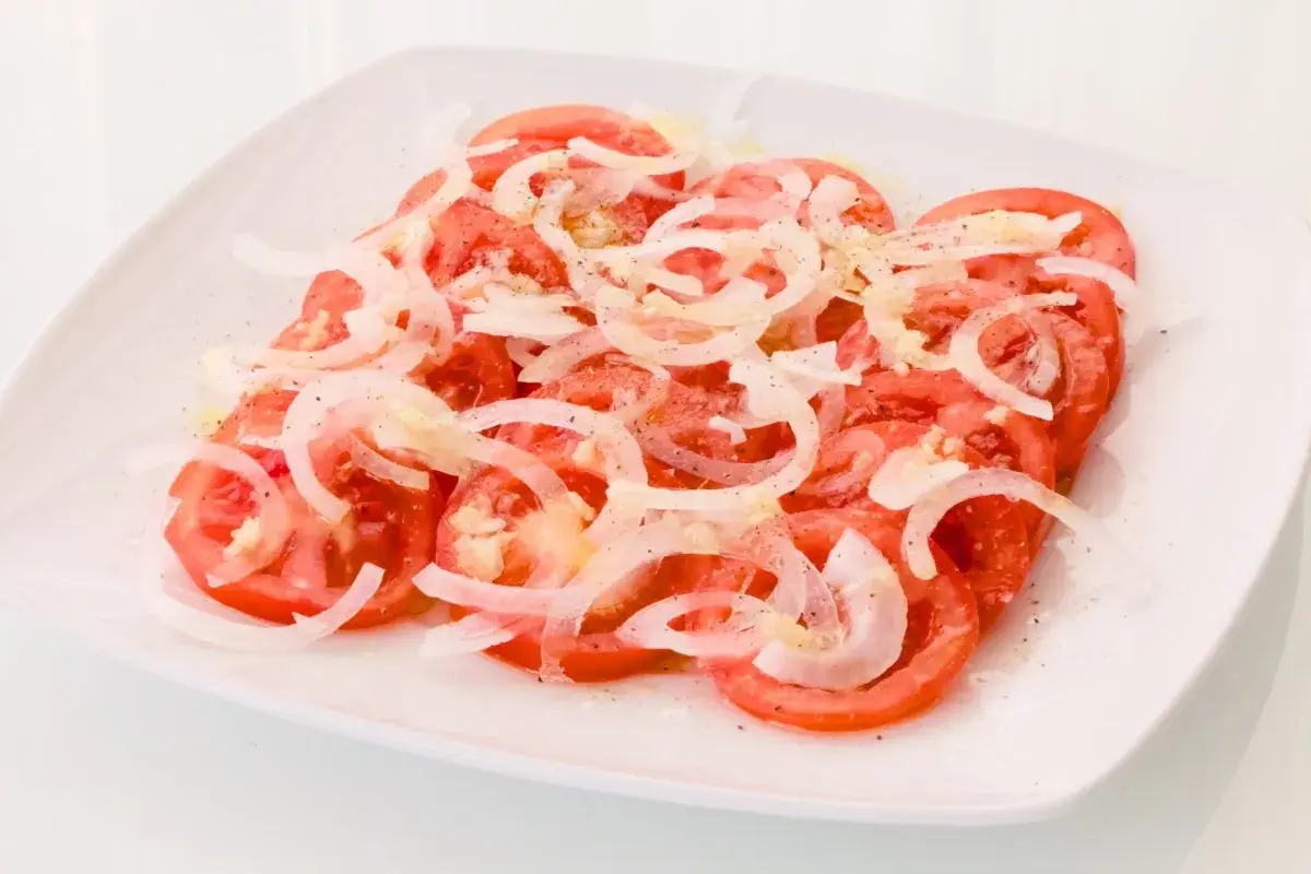 Una refrescante ensalada de tomate y cebolla, aderezada con sal y pimienta, lista para disfrutar.