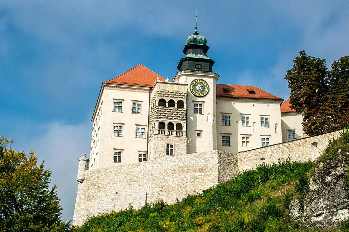 Zamek na Pieskowej Skale, biały z czerwonym dachem, z wieżą zegarową, na tle błękitnego nieba.