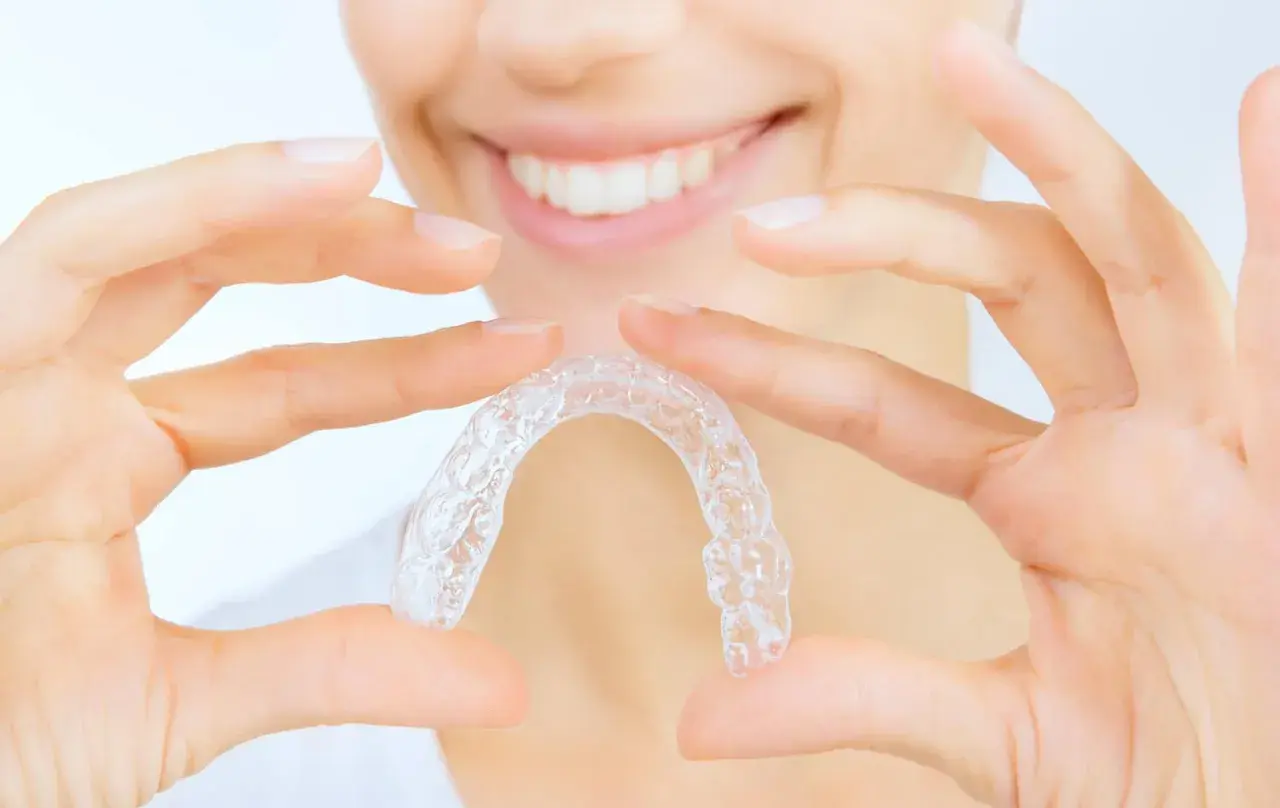 Manos sostienen un alineador transparente, mostrando cómo quitar Invisalign para una sonrisa perfecta.