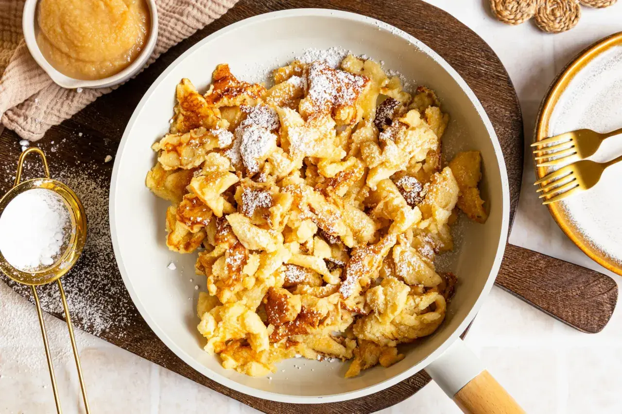 Kaiserschmarrn ohne Ei, fluffig und goldbraun, mit Puderzucker bestäubt. Dazu Apfelmus und zwei Gabeln.