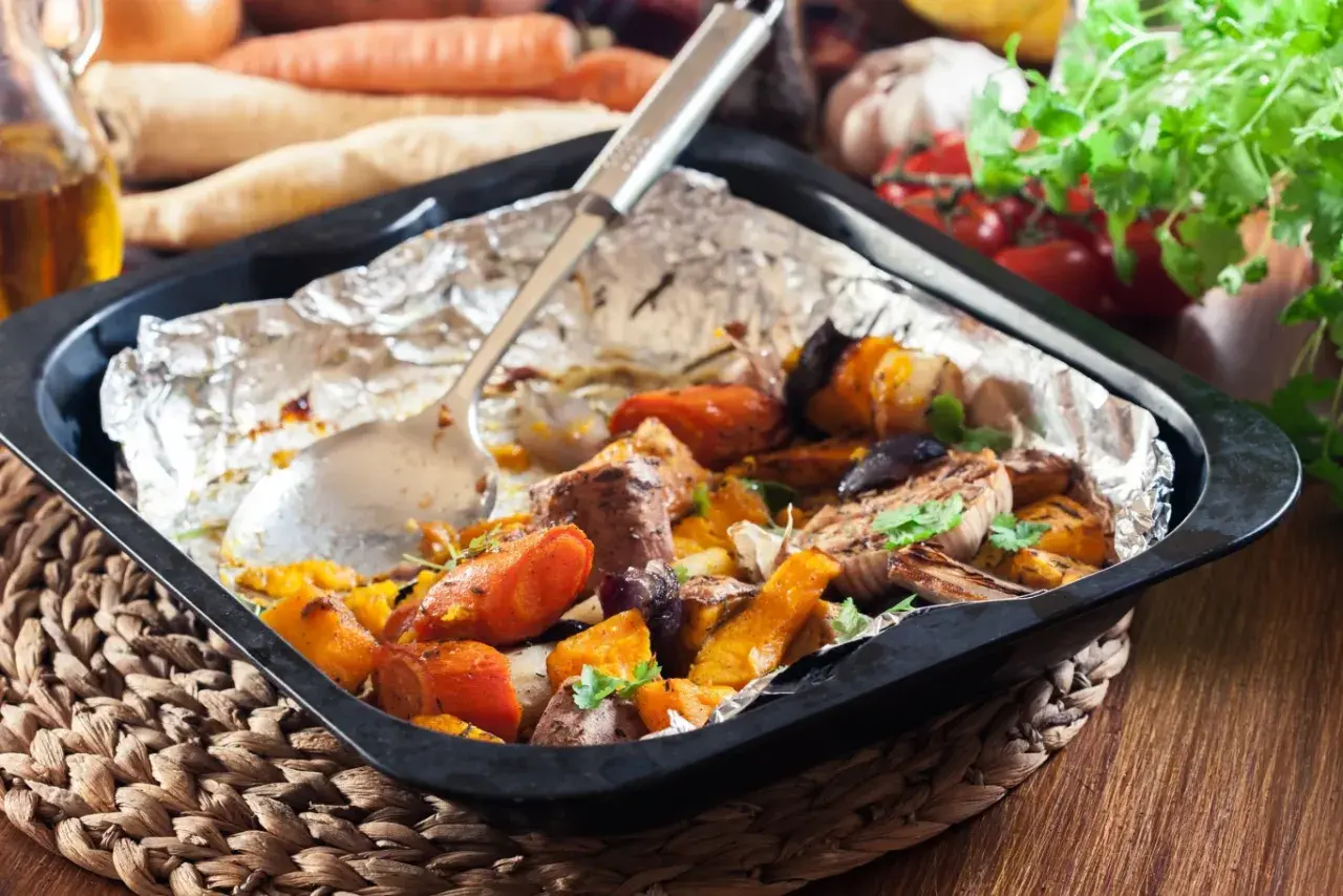 Szybkie danie z piekarnika: pieczone warzywa korzeniowe, dynia i mięso w folii aluminiowej, gotowe do podania.