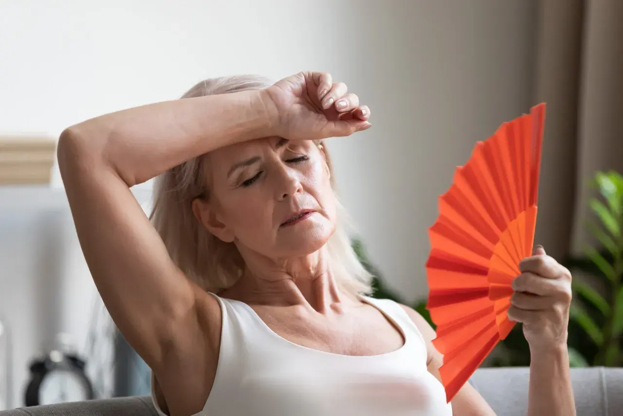 Frau fächelt sich mit einem orangefarbenen Fächer Luft zu, um etwas gegen Hitzewallungen zu tun.