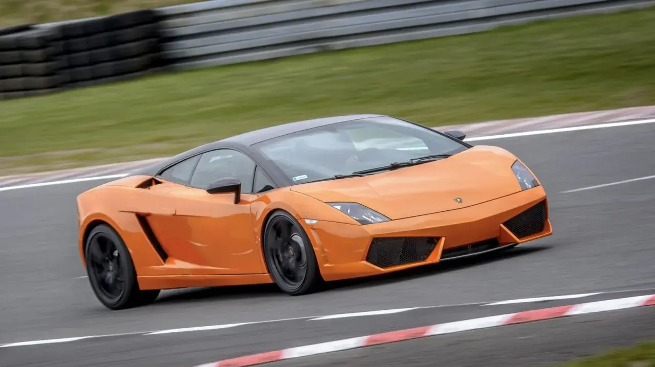 Pomarańczowe Lamborghini pędzi po torze wyścigowym, zostawiając za sobą smugę prędkości.