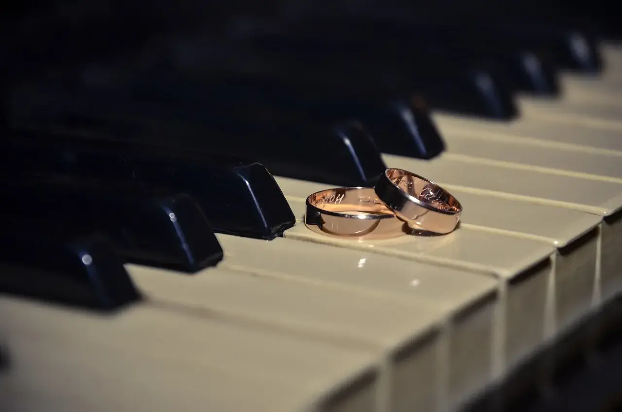 Dos alianzas de oro descansan sobre teclas de piano, evocando la pregunta: ¿cuanto pesa una alianza de oro?