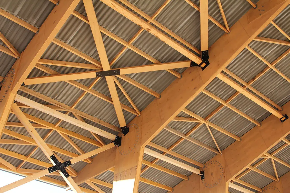 Structure complexe de poutres en bois de type **lvl bois**, soutenant un toit ondulé.