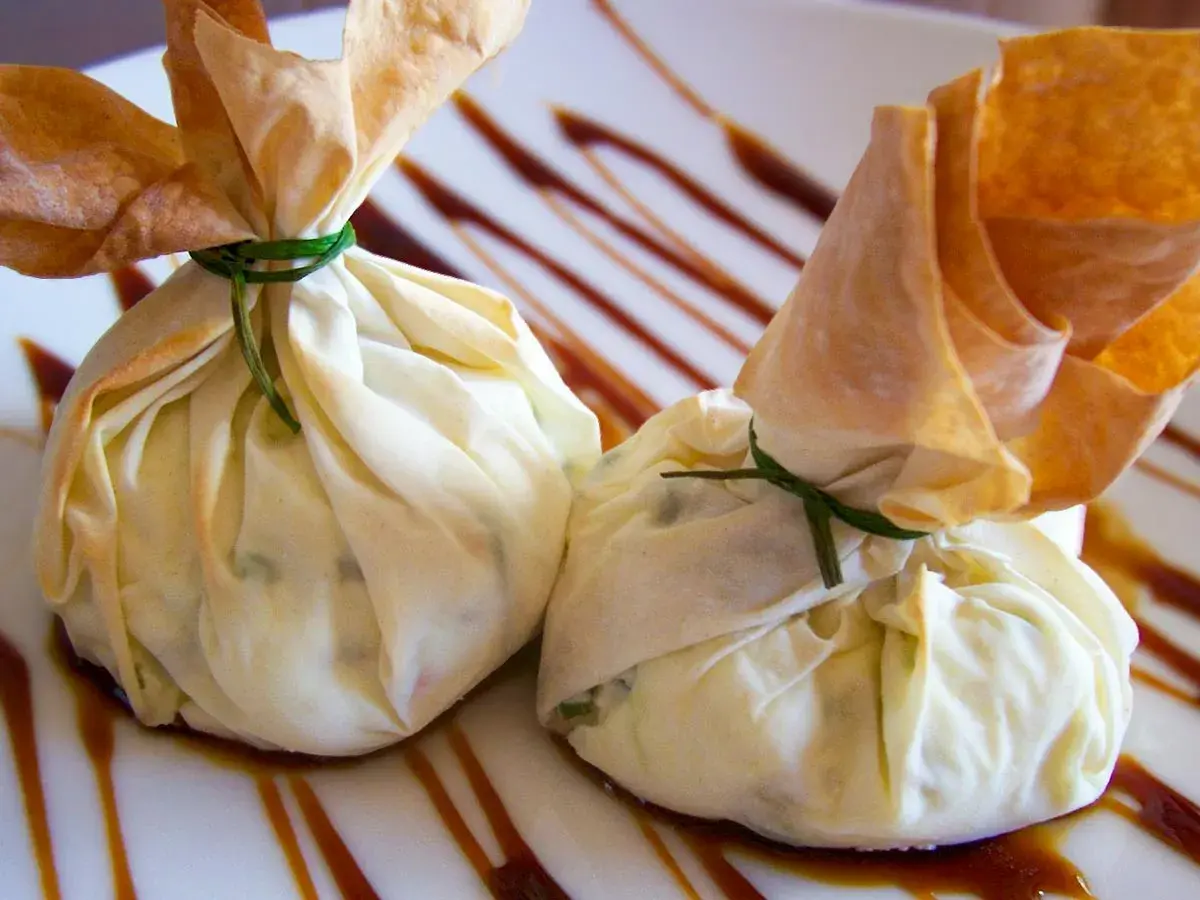Dos saquitos de pasta filo rellenos, atados con hilo verde, reposan sobre un plato con un glaseado oscuro.
