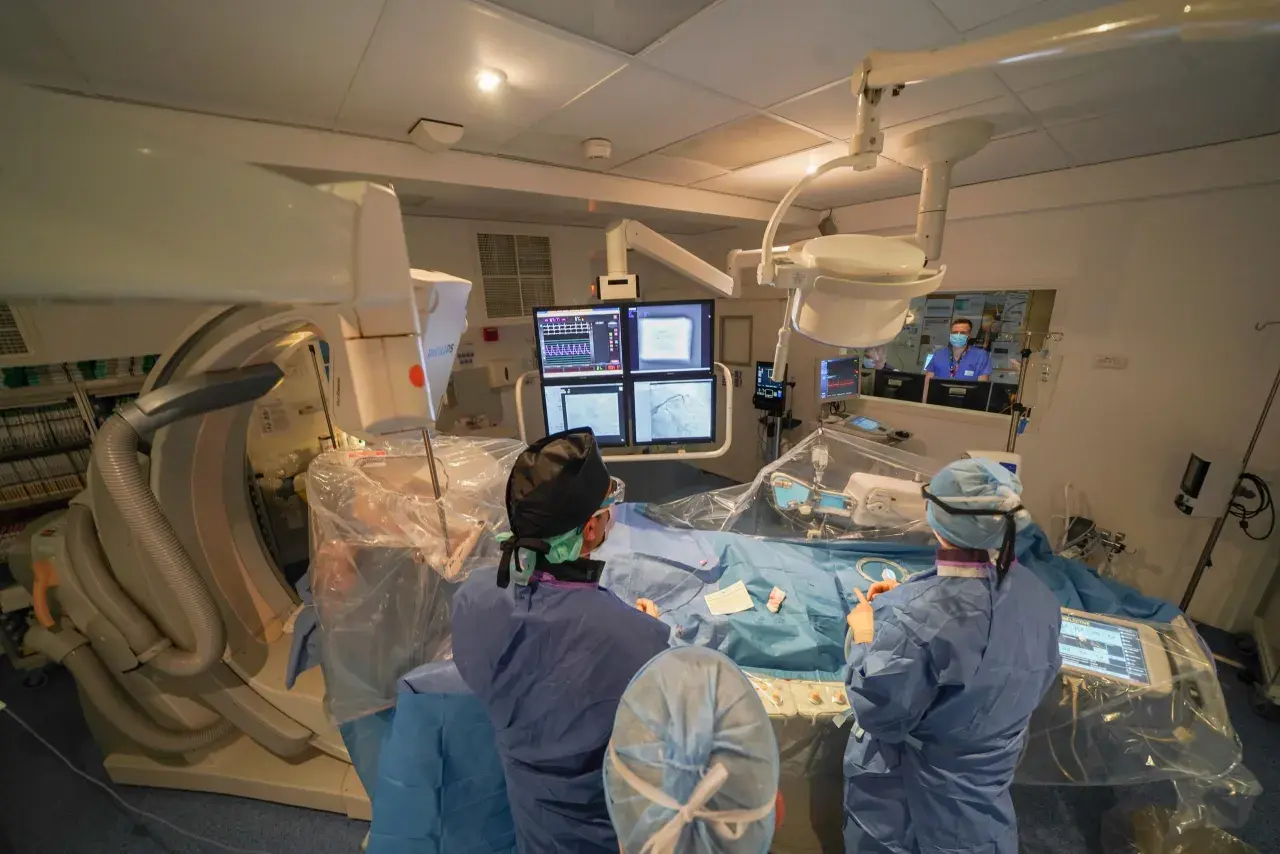 Équipe médicale en salle d'angiographie, préparant le repos après une coronarographie. Moniteurs affichant des images cardiaques.